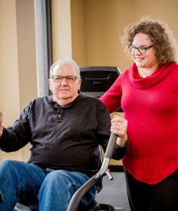 Female physical therapist assists older man on exercise machine