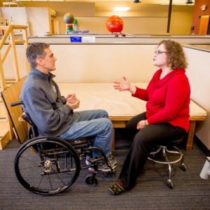 Female therapist sits across from man in wheelchair