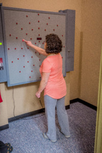 Woman in coral shirt uses the Dynavision device to strengthen hand-eye coordination