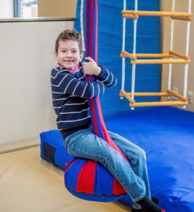 Young boy smiling swinging on an indoor swing during therapy