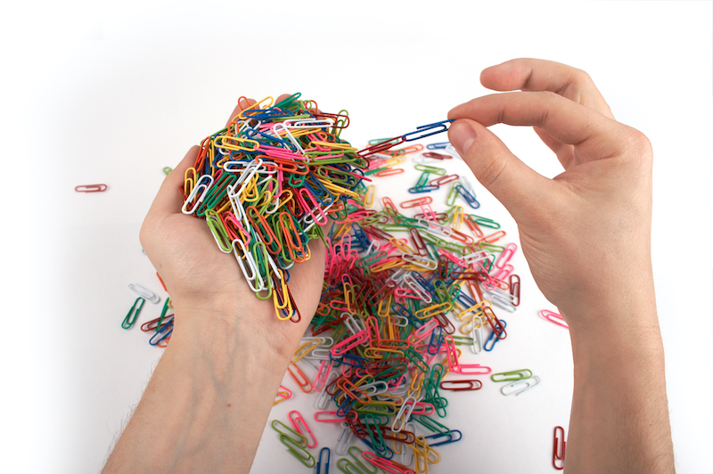 Adult hands make a paperclip chain with large handful of colored paperclips