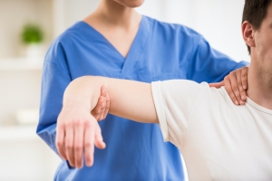 Female physical therapist wearing blue scrubs helps a male patient with shoulder mobility