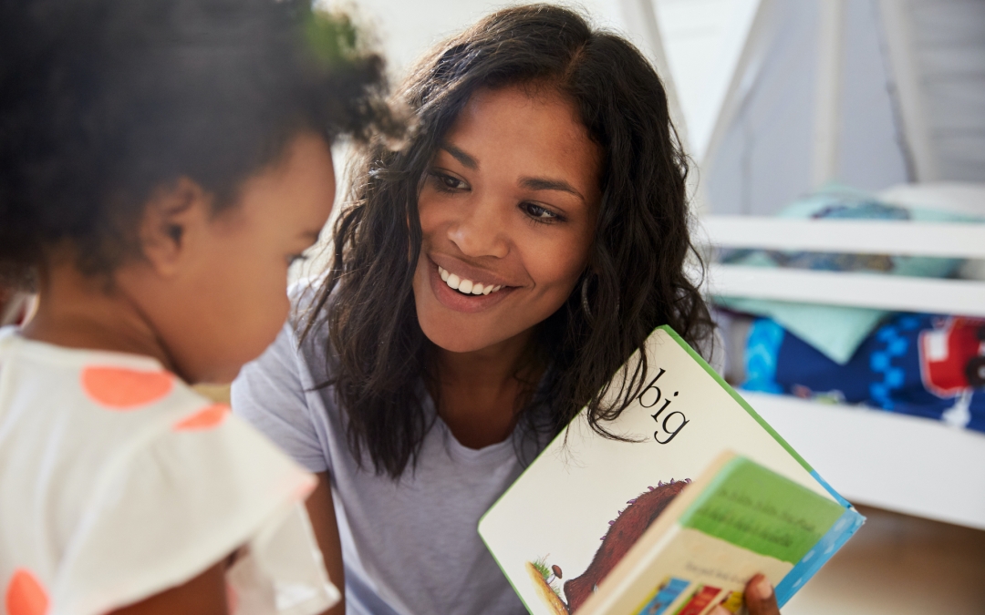 Black mom reads to daughter pointing out words and pictures in playroom