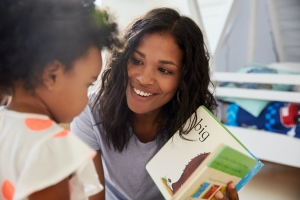 Black mom reads to daughter pointing out words and pictures in playroom